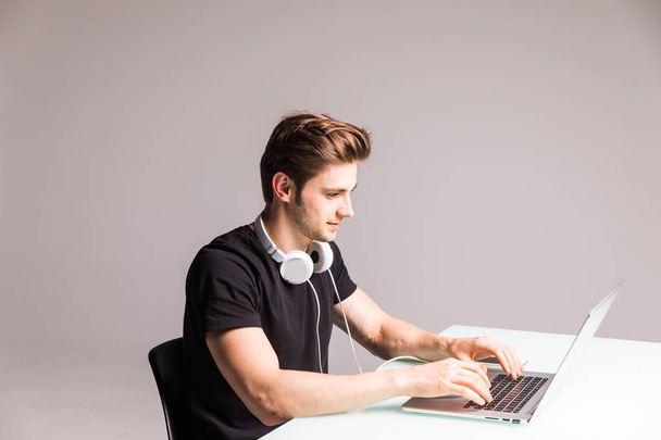 Εικόνα ενός νεαρού άνδρα στο γραφείο του υπολογιστή λειτουργεί σε φορητό υπολογιστή με ακουστικά σε λευκό - Φωτογραφία, εικόνα