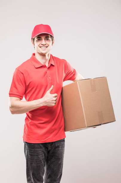 Uomo di consegna in uniforme rossa con pollici in su con scatola in mani isolate su bianco
 - Foto, immagini