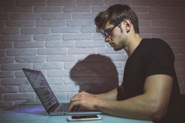 Un joven que trabaja en la computadora por la noche en una oficina oscura. El diseñador trabaja en el tiempo posterior.  - Foto, Imagen