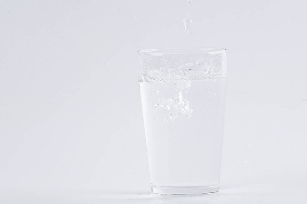 Water pouring into clear glass over white background - Photo, Image