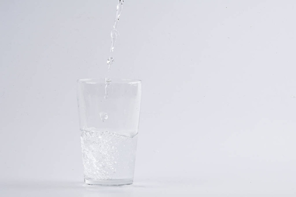 Agua que vierte en vidrio transparente sobre fondo blanco
 - Foto, imagen