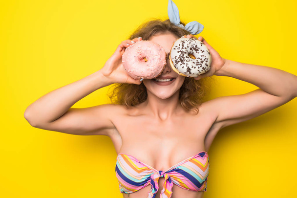 Portrait of happy hipster curly girl choosing beetwen two donutes on yellow background - Foto, Imagem
