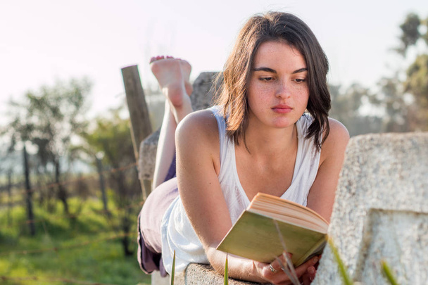 Menina que coloca ao ar livre livro de leitura
 - Foto, Imagem