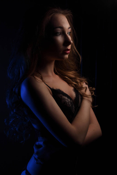 Sexy young beautiful woman with curls in sensual black lingerie, lighted with blue in studio portrait - Photo, Image