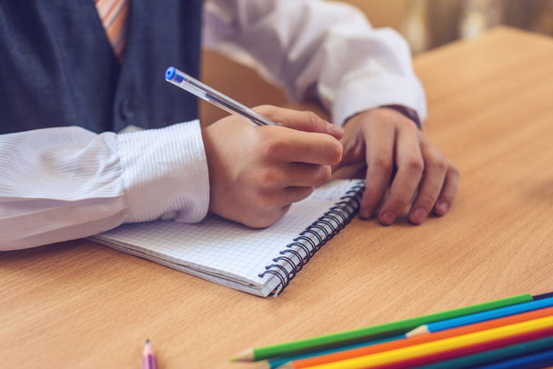 Powrót do szkoły. Słodkie dziecko siedzi przy biurku w klasie. Chłopiec jest nauka, lekcje pisze długopisem w Notatniku - Zdjęcie, obraz
