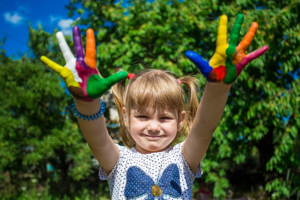 Χαριτωμένο κορίτσι που δείχνει τα χέρια της βαμμένα σε έντονα χρώματα. Χέρι εκτυπώσεις. - Φωτογραφία, εικόνα