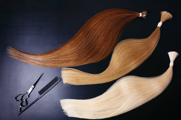 наращивание волос трех цветов на темном фоне с помощью ножниц и гребня. copyspace top view
. - Фото, изображение