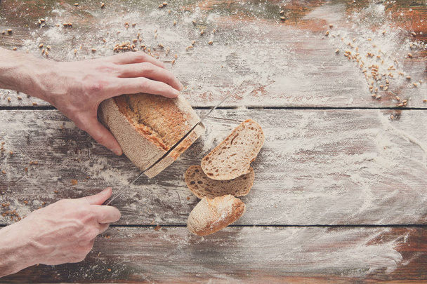 Bakery concept background. Hands cutting bread loaf slices - Photo, Image