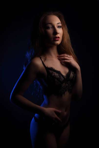 Sexy young beautiful sensual woman with curls in sensual black lingerie, lighted with blue in studio - 写真・画像