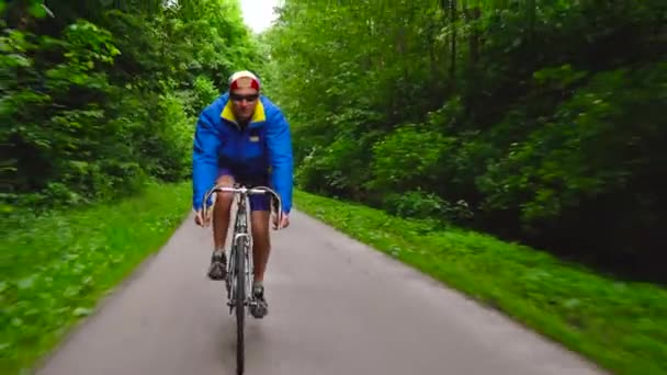 Man van middelbare leeftijd is een racefiets langs een bos weg rijden - Video