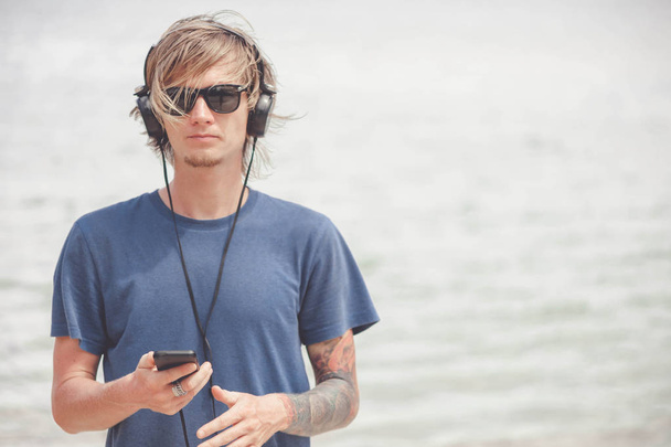 Portrait of young man in headphones and sunglasses at the beach - Photo, Image