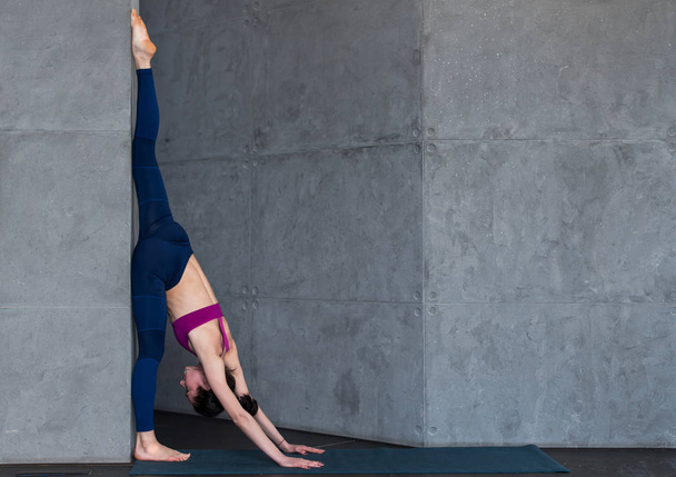 Gimnasta profesional haciendo ejercicio de estiramiento de calentamiento realizando de pie dividido contra la pared en el estudio
 - Foto, Imagen