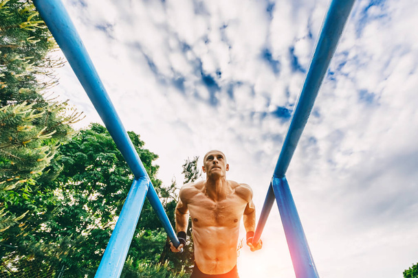 Bald Man doing push ups on parallel bars in a park - Photo, Image