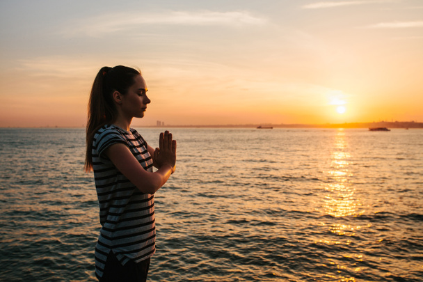 Young beautiful girl practicing yoga and meditation next to the sea at sunset. Sport. Yoga. Meditation. Recreation. Vacation. Relaxation. - Photo, Image