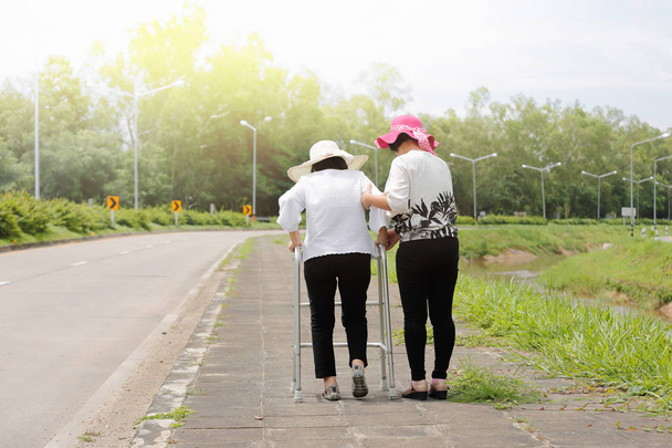 Tochter kümmert sich um ältere Frau, die bei starker Sonne auf Straße läuft - Foto, Bild
