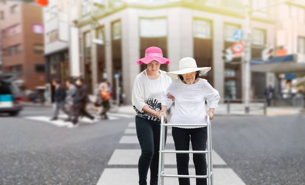 Fille prendre soin femme âgée marche à travers la rue dans le centre-ville
 - Photo, image