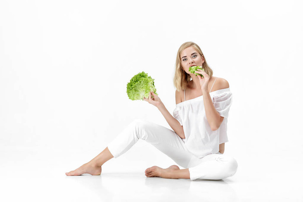Beautiful blond woman in white blouse eating fresh green salad on white background. Health and Diet - 写真・画像