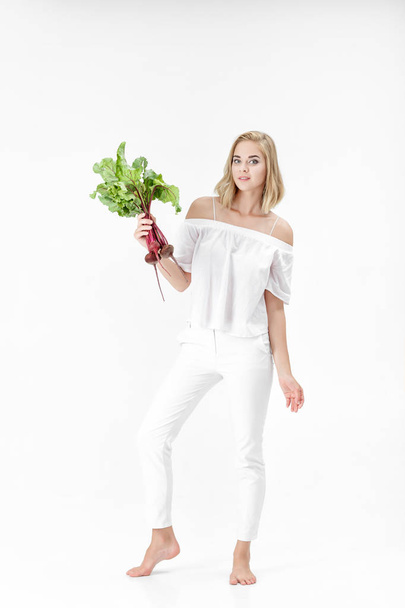 Beautiful blond woman holds beetroot with green leaves on white background. Health and vitamins - Foto, Bild