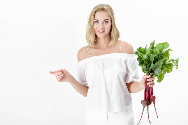 Beautiful blond woman holds beetroot with green leaves on white background. Health and vitamins - Fotoğraf, Görsel