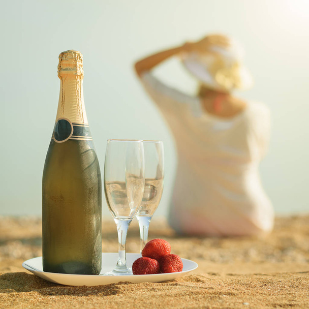 Een fles champagne, bril en aardbeien op de achtergrond van de vrouwen. - Foto, afbeelding