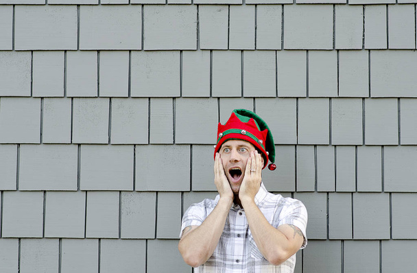 Döbbenve ember karácsonyi kalap és egy szürke háttér. - Fotó, kép