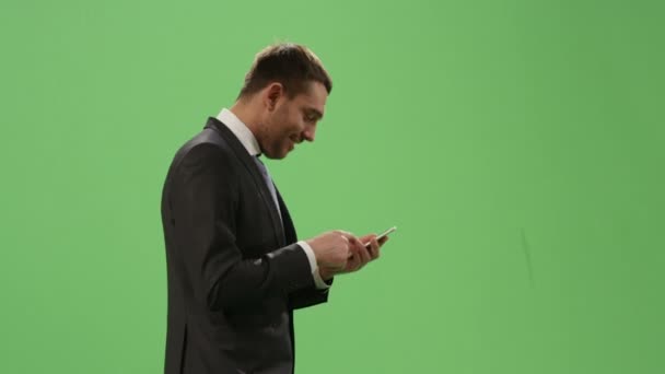 Businessman in a suit is using a smartphone while walking on a mock-up green screen in the background. - Séquence, vidéo
