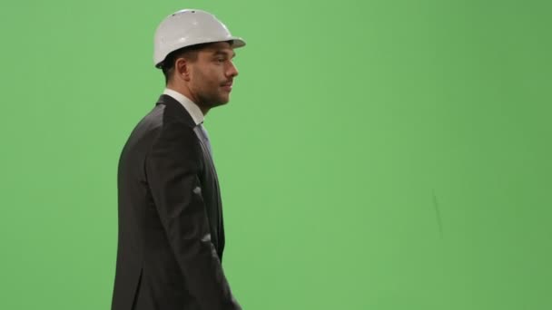 Businessman in a hard hat and a suit is walking on a mock-up green screen in the background. - Filmati, video