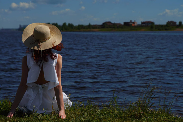 Woman in white dress sits on riverside, back view - Foto, afbeelding