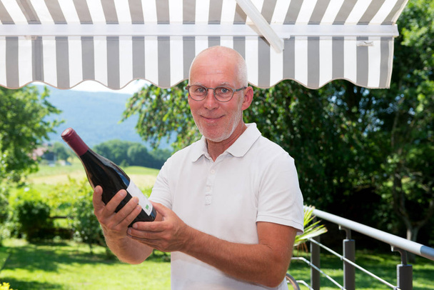 hombre maduro con botella de vino tinto, en la terraza
 - Foto, imagen