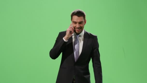 Businessman in a suit is walking and talking on mobile phone on a mock-up green screen in the background. - Кадри, відео