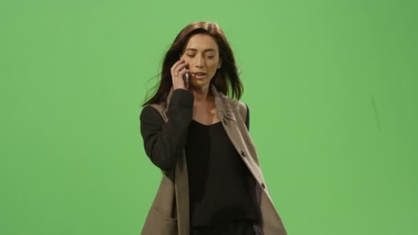 Casual brunette woman is walking and talking on the phone on a mock-up green screen in the background. - Materiał filmowy, wideo
