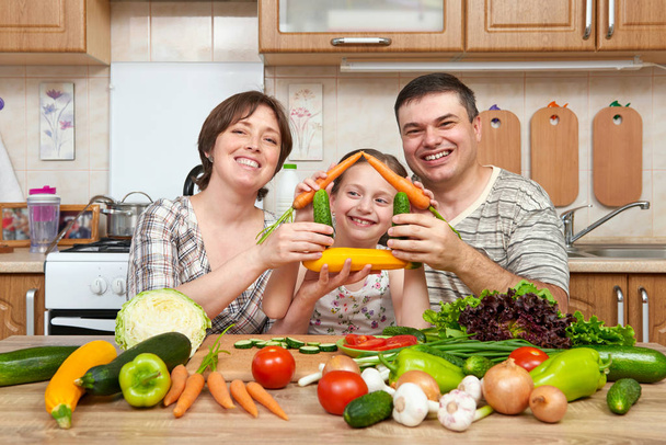 Family cooking in kitchen interior at home, fresh fruits and vegetables. Healthy food concept. Woman, man and children. Making house shape from vegetables. - Photo, Image