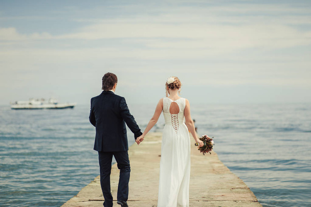 Esküvő házaspár egy sétára menyasszony és a vőlegény tengeri naplemente építészeti fű, homok - Fotó, kép