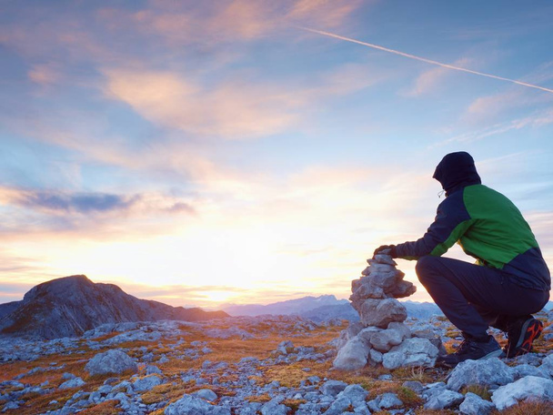 Alleen wandelaar man op de bovenkant van de Alpine gebergtevorming pyrmid van steentjes. - Foto, afbeelding