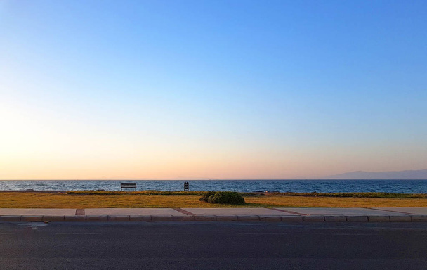 Tengerre néző útról egy üres pad és egy magányos bokor naplemente előtt - Fotó, kép