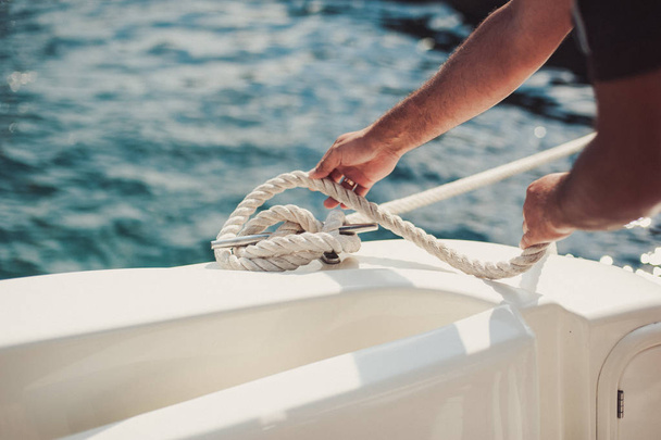 людина зав'язує вузол і закріплює швартування для своєї хобі яхти вітрильного човна
 - Фото, зображення