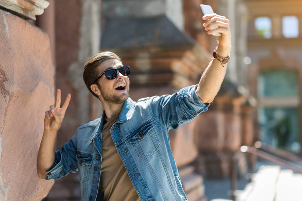 Cheerful youthful man using gadget while sightseeing - Fotó, kép