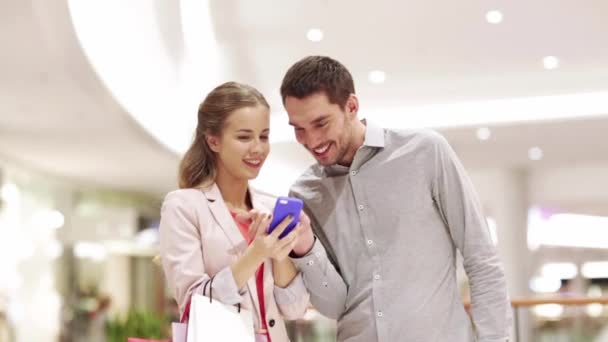 couple with smartphone and shopping bags in mall - Filmati, video