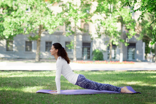 A sports woman on a sunny urban background. A beautiful and balanced lady practicing yoga. A slim female practicing asanas.  - Фото, изображение