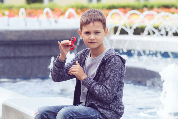 Boy with a fidget spinner sitting in city park - Фото, изображение