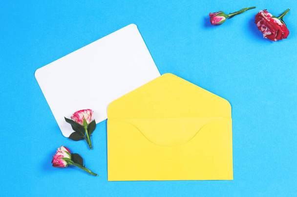 Puste karty z pozdrowieniami z żółtą kopertę i różowe kwiaty róży na niebieskim tle - Zdjęcie, obraz