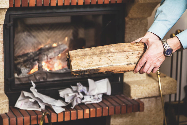 Hands of man holding piece of wood in front fireplace - Foto, Imagem