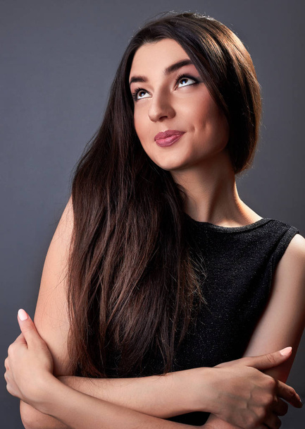 Portrait of surprised young lady in black dress with a beautiful hair on gray background.Emotion portrait - Foto, Imagen