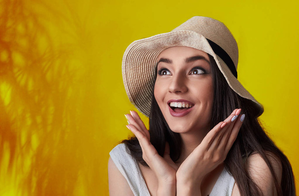 Portrait of surprised a smiling pretty girl in summer hat posing isolated over yellow tropic background.Cocnept summer discout.Shocked - 写真・画像