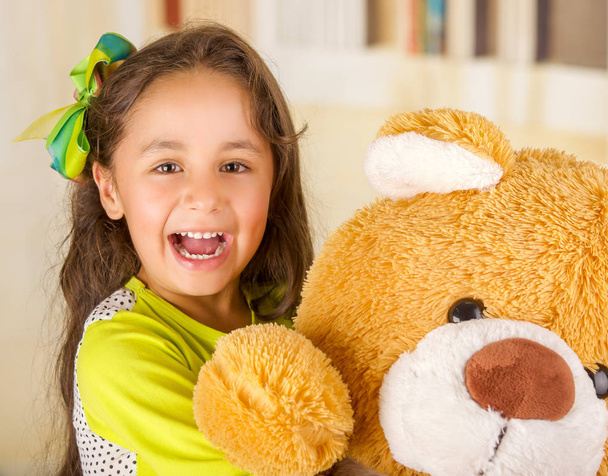 A portrait of a young pretty girl smiling and hugging her teddy bear over blurred background - Foto, immagini