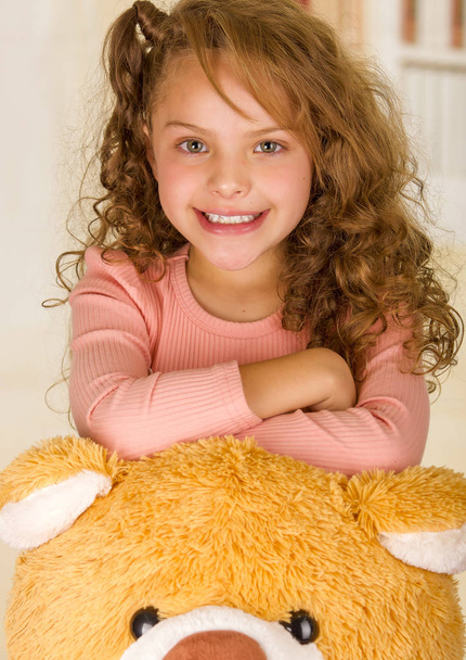 A portrait of a young pretty girl smiling and posing over her teddy bear head in a doctor office background - Foto, imagen