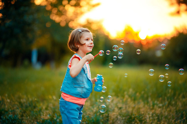 Five years old caucasian child girl blowing soap bubbles outdoor at sunset . - Φωτογραφία, εικόνα