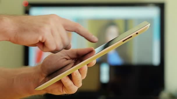 Primer plano de la mano masculina usando una tableta IPad en casa en el fondo de la TV
 - Metraje, vídeo