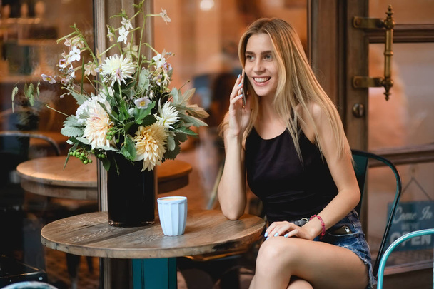 彼女の友人とスマート電話で話しの屋外カフェに座っている女性 - 写真・画像
