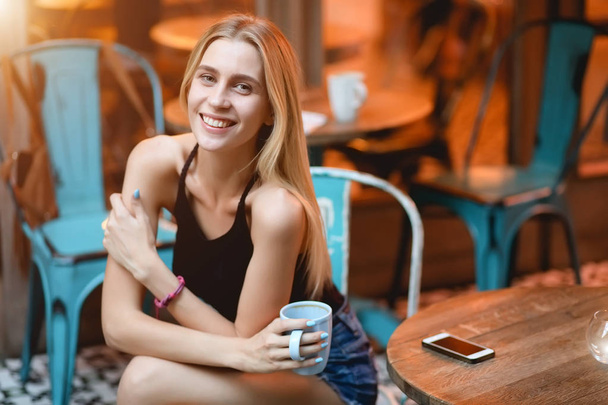 Woman sitting in a cafe drinking delicious latte. Coffee break outdoors in evening. She smile. - Foto, Imagem